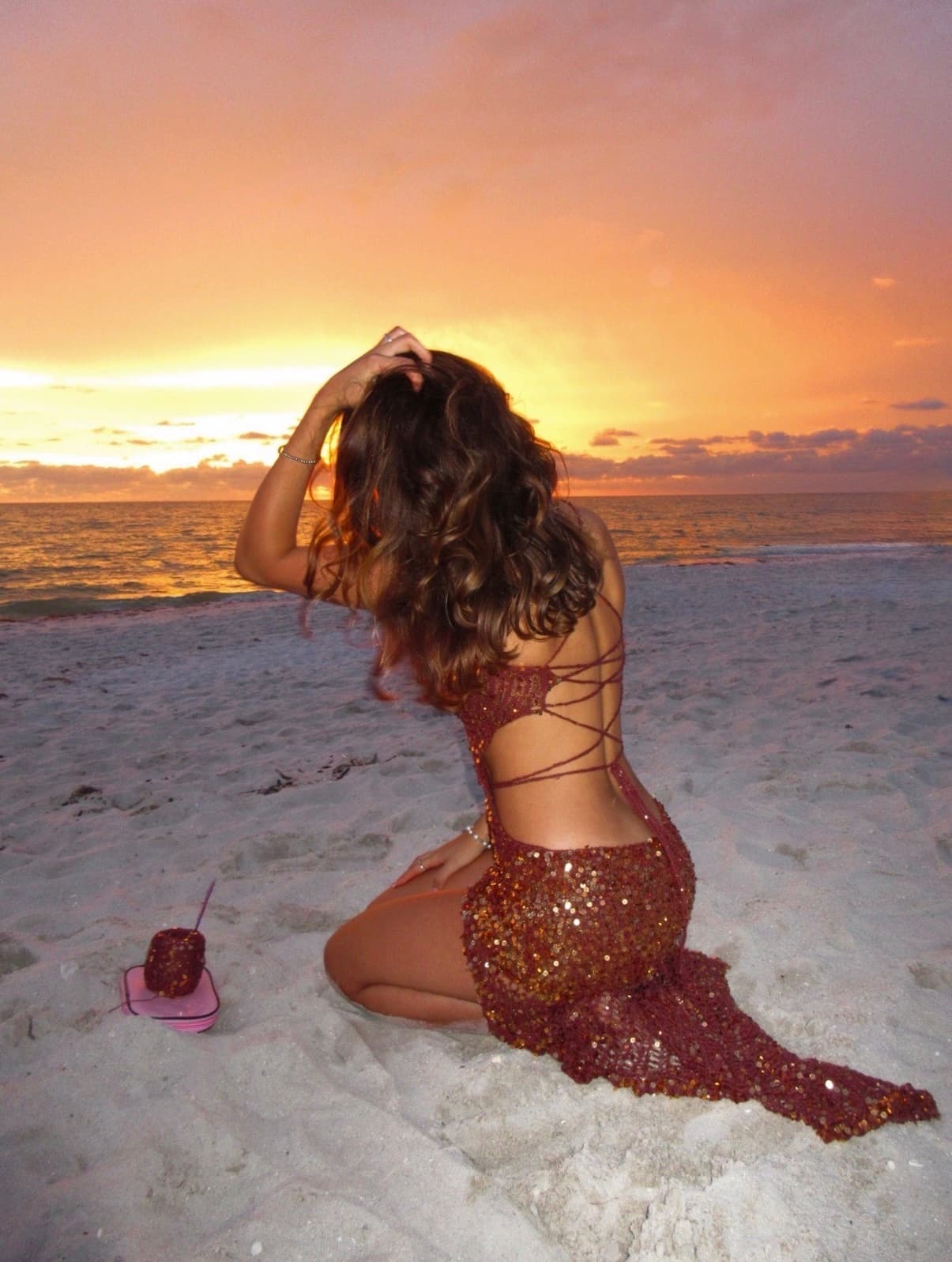 The sequin crochet gown photographed from behind while seated on the beach at sunset.