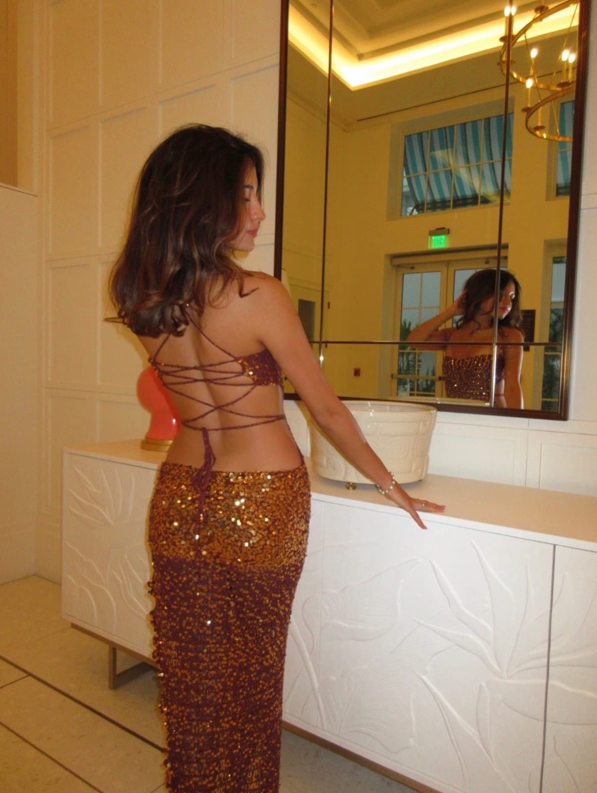 The burgundy sequin crochet gown photographed from behind in a mirrored interior.